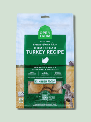 Package of Open Farm Freeze Dried Patties Raw Homestead Turkey Recipe dog food, featuring green and brown design elements, images of a farm field and a dog, and labels such as "Humanely Raised & Sustainably Sourced" and "Dinner Patties."