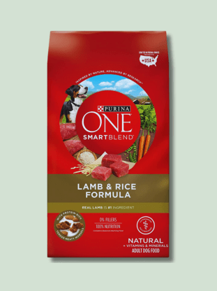 A red package of Purina ONE SmartBlend natural adult dog food with a lamb and rice formula. The package has images of raw lamb cuts, rice, and a dog surrounded by greenery.