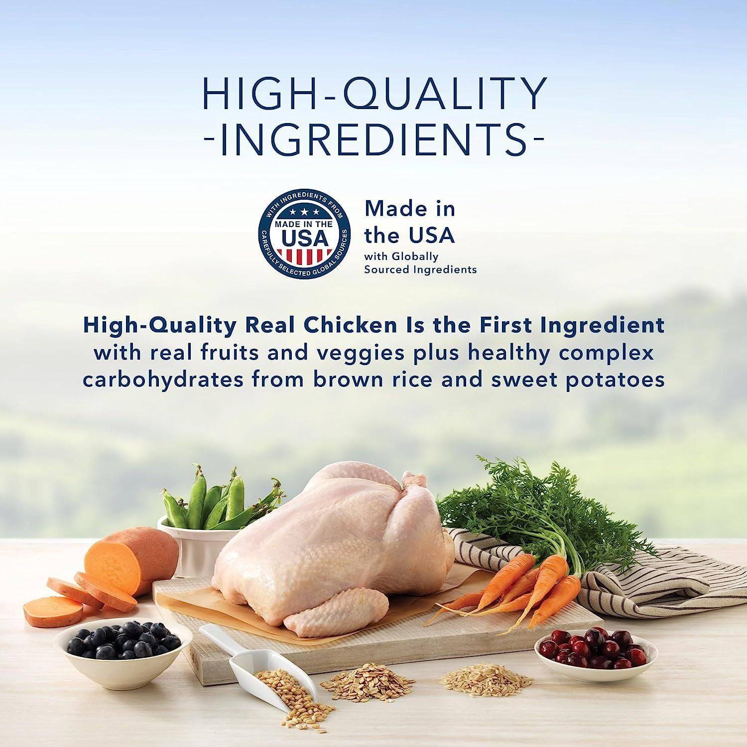 An advertisement for high-quality ingredients with a raw whole chicken, carrots, sweet potatoes, cranberries, blueberries, brown rice, and greens displayed on a wooden cutting board. A seal states "Made in the USA with Globally Sourced Ingredients." A text overlay reads "High-Quality Real Chicken Is the First Ingredient with real fruits and veggies plus healthy complex carbohydrates from brown rice and sweet potatoes."