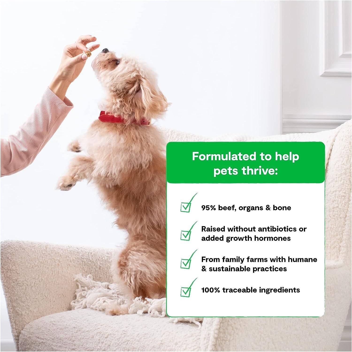 A small, fluffy tan dog standing on its hind legs being fed by a human hand, next to a green sign listing the benefits of a pet food product, with a light interior background.