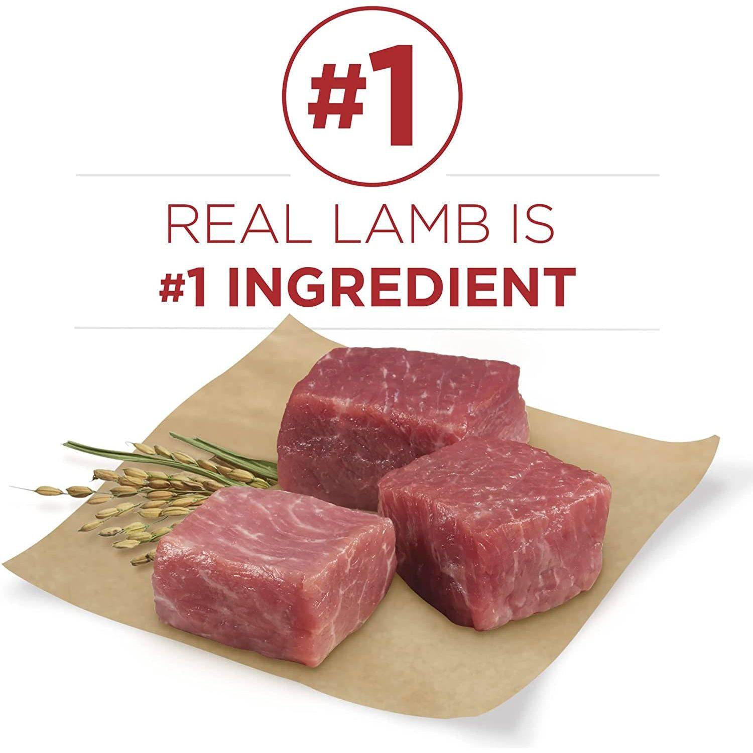 Three cubes of raw lamb meat on a piece of brown paper with a few stalks of wheat, accompanied by a red circular tag with white text that reads "#1 REAL LAMB IS #1 INGREDIENT".