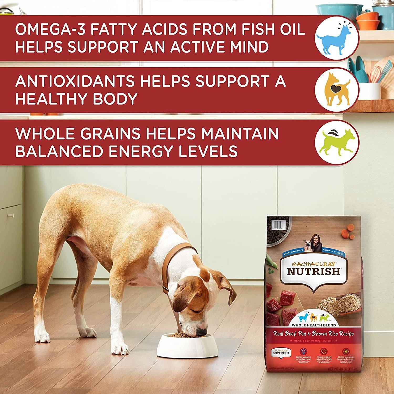 A brown and white dog is eating from a bowl in a kitchen-like setting next to a bag of Rachael Ray Nutrish dog food with labels highlighting Omega-3 fatty acids from fish oil for an active mind, antioxidants for a healthy body, and whole grains for balanced energy levels.