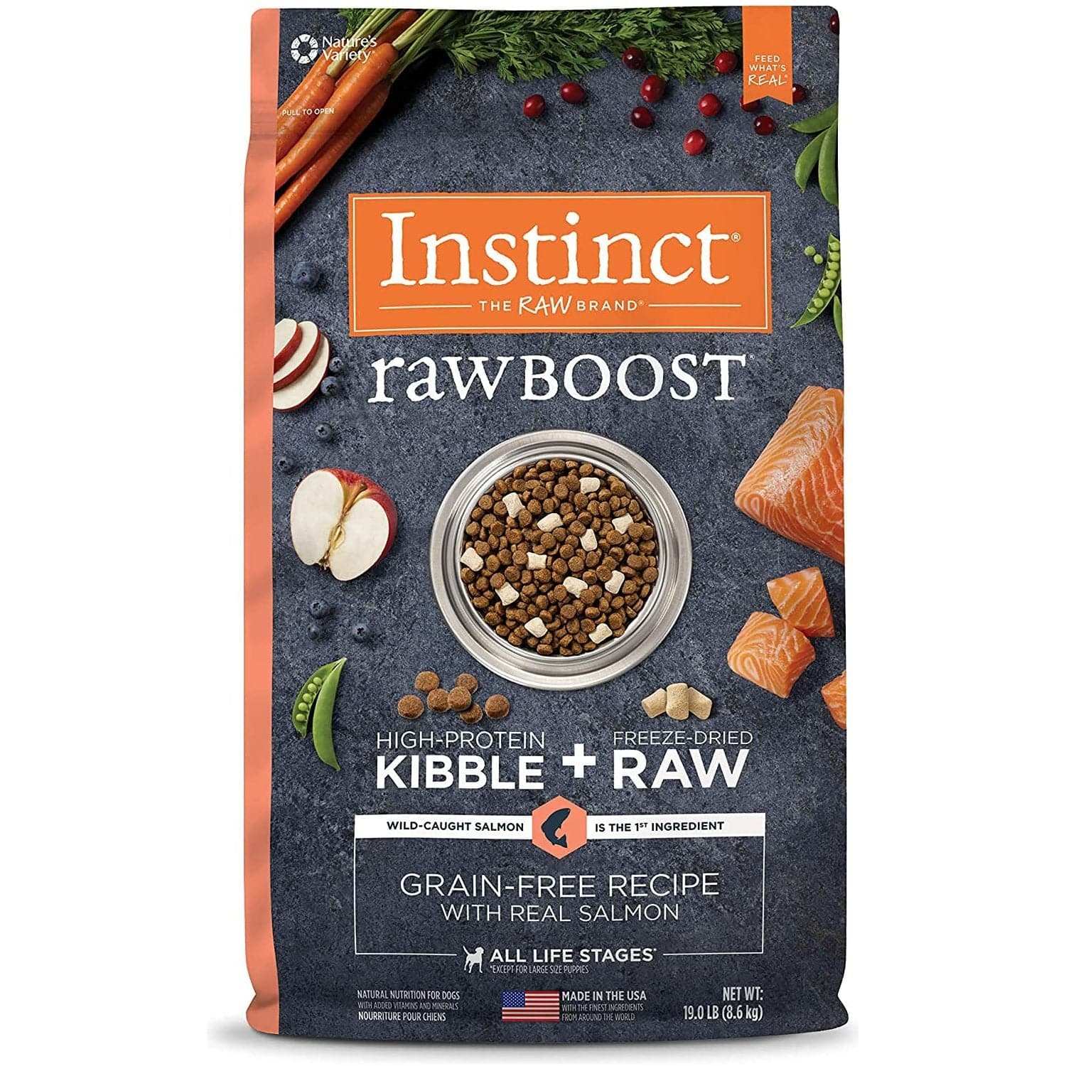 Packaging of Instinct Raw Boost high-protein dog food featuring freeze-dried kibble and raw salmon pieces, displayed with visuals of salmon, sliced apple, and vegetables around a bowl of the product on a slate background.