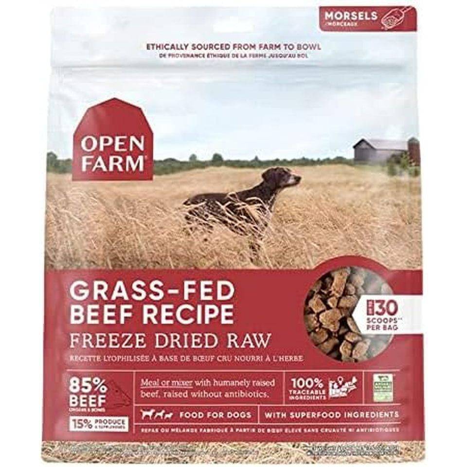 A bag of Open Farm dog food with the label "Grass-Fed Beef Recipe Freeze Dried Raw". The upper part of the bag features a pastoral scene with a dark-colored dog lying in a field, a red barn-like icon, and mentions ethical sourcing. The lower part includes details on ingredients and health benefits, such as "85% beef, 15% produce", "humanely raised beef" and "100% traceable ingredients".