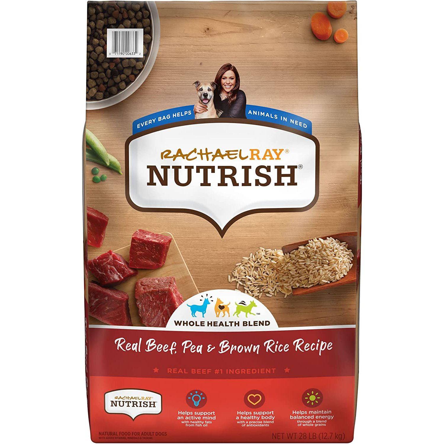 A bag of Rachael Ray Nutrish Whole Health Blend with Real Beef, Pea & Brown Rice Recipe dog food, highlighting real beef as the number one ingredient. The package features an image of a dog, with visual elements illustrating support for an active mind, healthy body, and balanced energy. It's a natural food for adult dogs, with a net weight of 28 lbs. On the wooden table around the bag are scattered ingredients like raw beef cubes, brown rice, peas, and a bowl full of dry kibble.