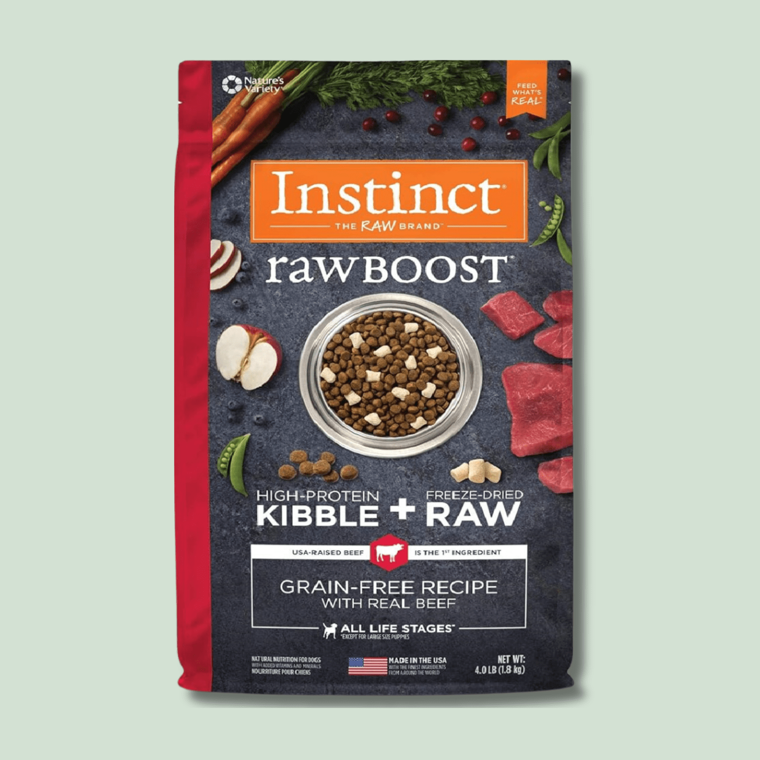 A package of "Instinct Raw Boost" high-protein kibble and freeze-dried raw beef dog food showing contents clearly displayed alongside fresh vegetables, garlic cloves, and berries on a grey surface. The bag is predominantly red and features the product logo along with details about the grain-free recipe for all life stages.